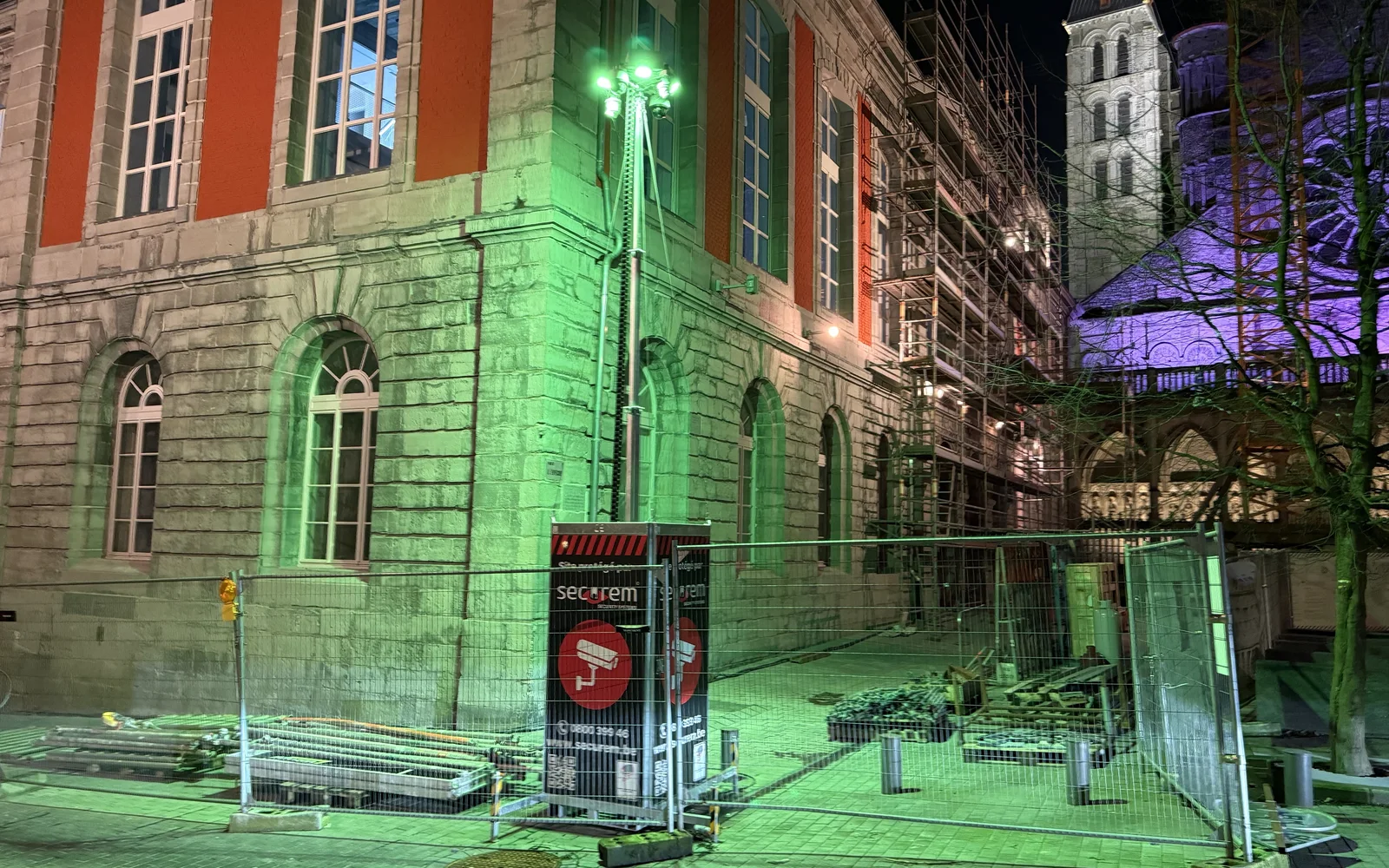 Mât Protect Mobile éclairé en vert, de nuit, devant un bâtiment en rénovation sous échafaudage