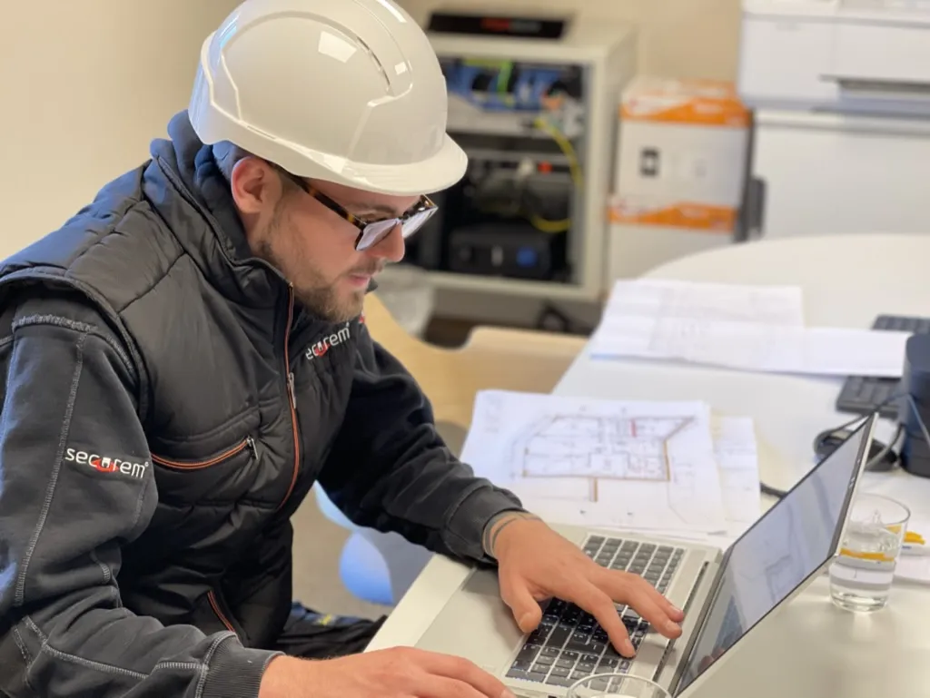 Technicien Securem préparant une installation sur plans, ordinateur portable ouvert